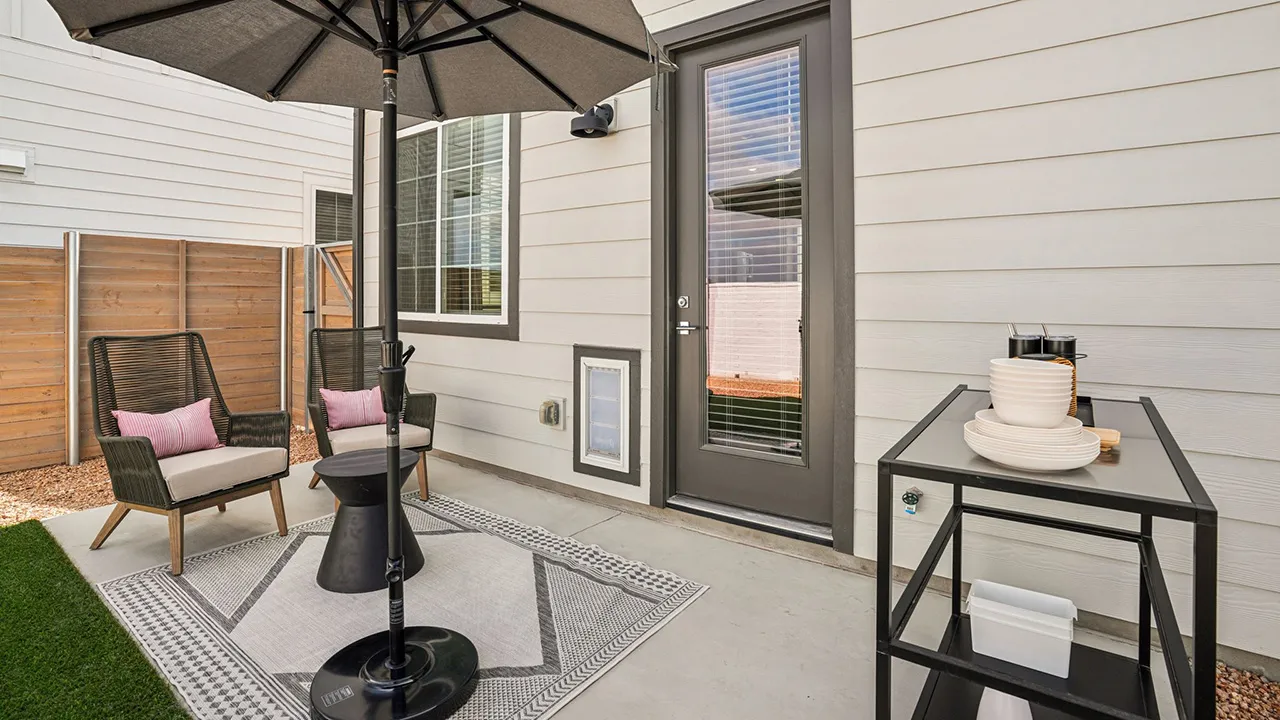 Backyard with  small artificial grass area, two chairs, table, and umbrella.