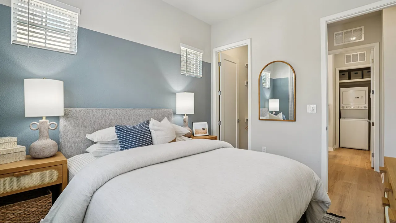 Modern bedroom with blue accent wall, bed with white bedding, two nightstands, and open door leading to laundry area.