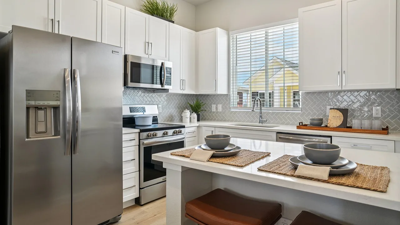 Modern kitchen with white cabinets, stainless steel appliances, and island with place settings. 