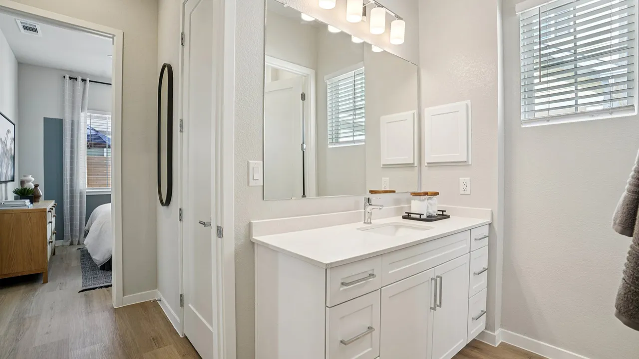 Modern bathroom with white vanity, white countertop, with view of a bedroom in the background.