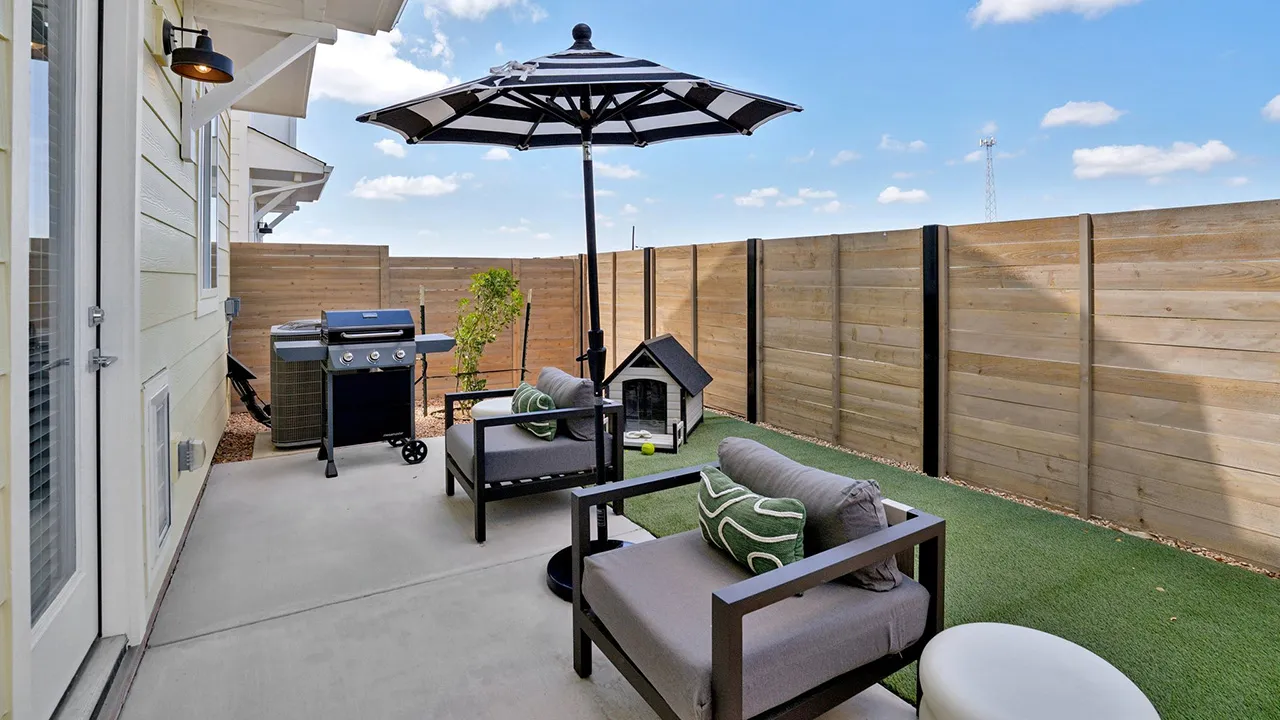 Outdoor patio with two gray cushioned chairs, black-and-white striped umbrella, grill, and dog house.