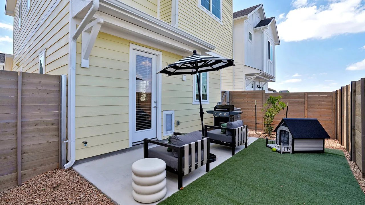 Outdoor patio with two gray cushioned chairs, black-and-white striped umbrella, grill, and dog house.