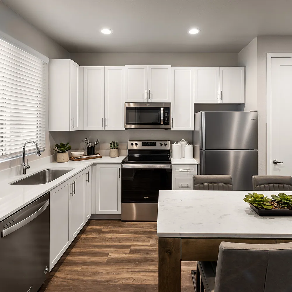 Modern kitchen with white cabinets, stainless steel appliances, wooden floor, and dining table with green centerpiece.
