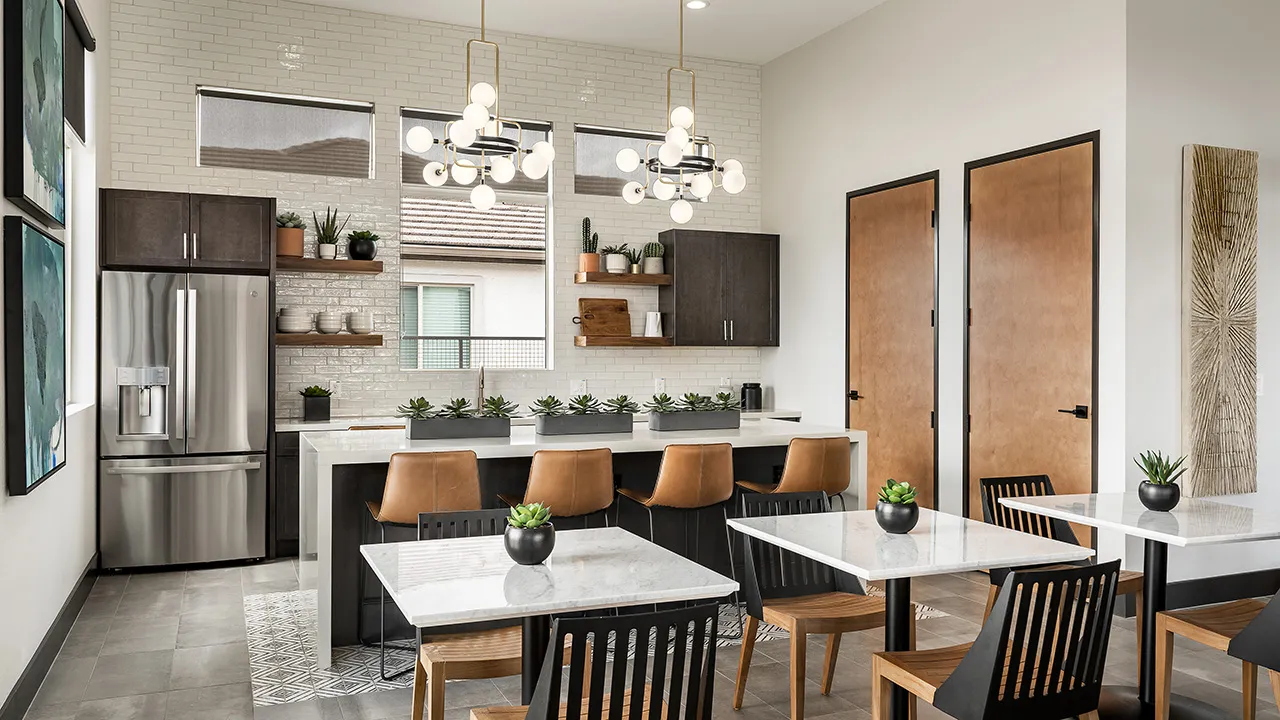 Modern kitchen with marble tables, brown chairs, stainless steel fridge, pendant lights, and decorative plants.