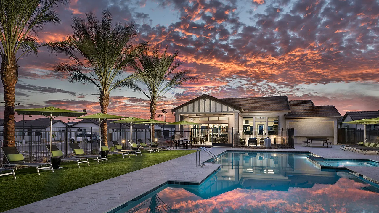 Residential pool and patio area with palm tree and colorful sunset sky reflecting in water.
