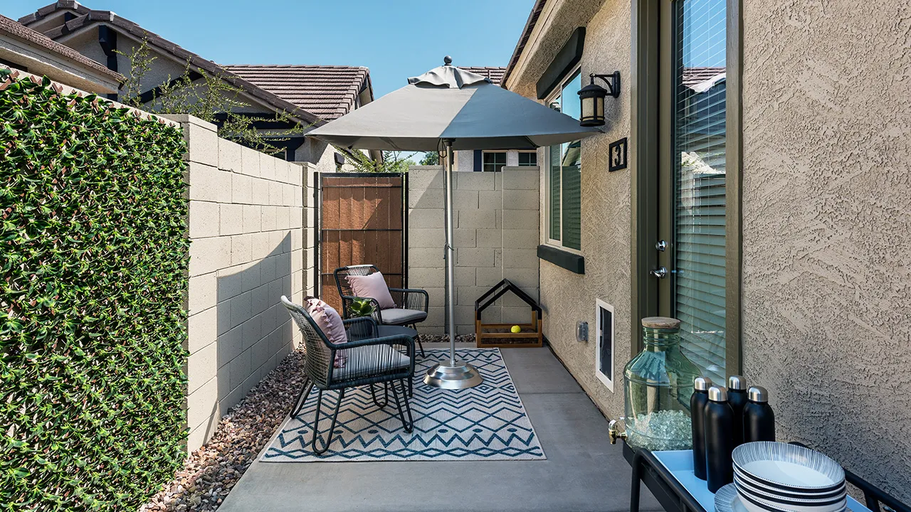 Cozy patio with two black chairs, pink cushions, umbrella, rug, and outdoor table with bottles and plates.