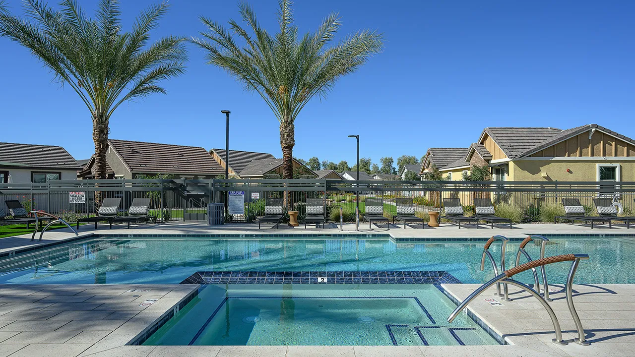 Residential outdoor pool with palm trees, lounge chairs, and clear blue sky in the background.