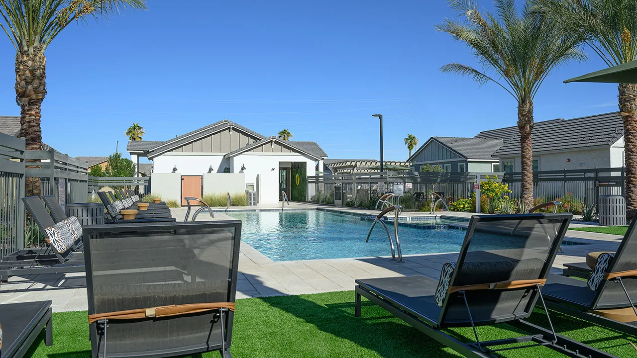Outdoor pool with black loungers and palm trees under a clear blue sky at a residential complex.