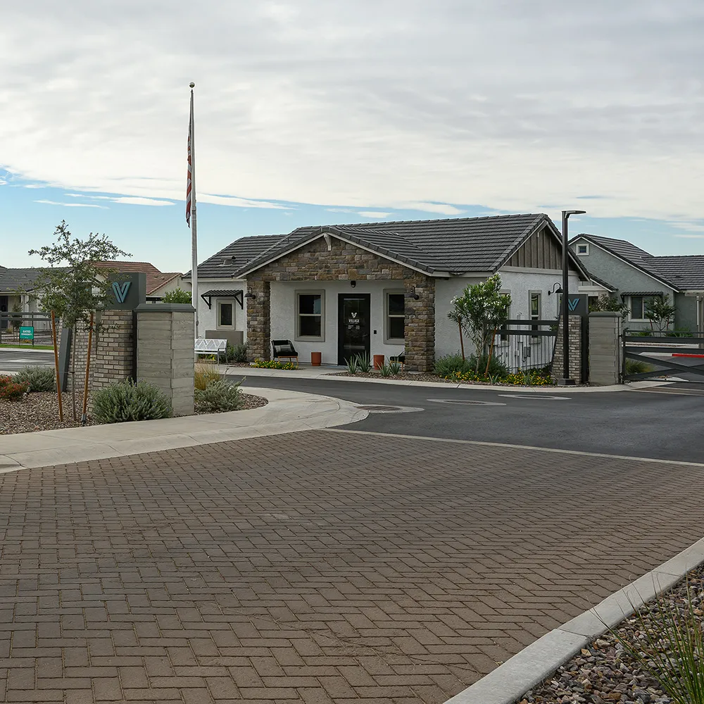 Entrance to Village at Schnepf Farms with signage, paved road, and office building under a cloudy sky.