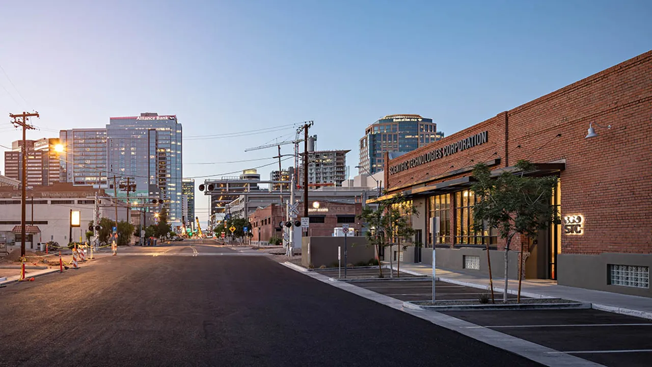 Brick building with large windows labeled 'Scientific Technologies'. View of Downtown Phoenix street and buildings at dusk. 
