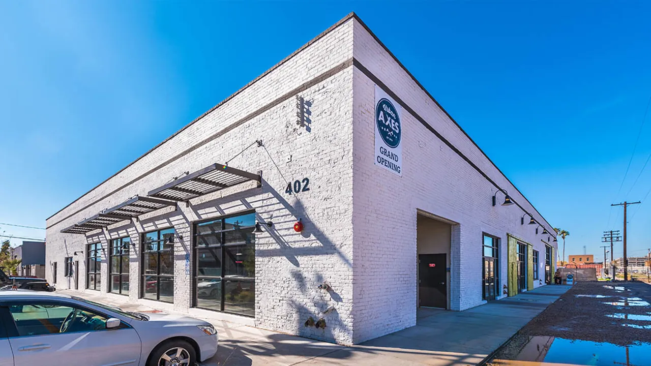 White one-story commercial warehouse building with the number 402 on the side and lime green utility doors and parking lot spaces.