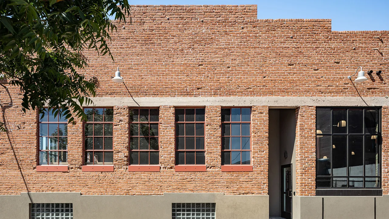 Street view of a red brick building with a row of large windows.
