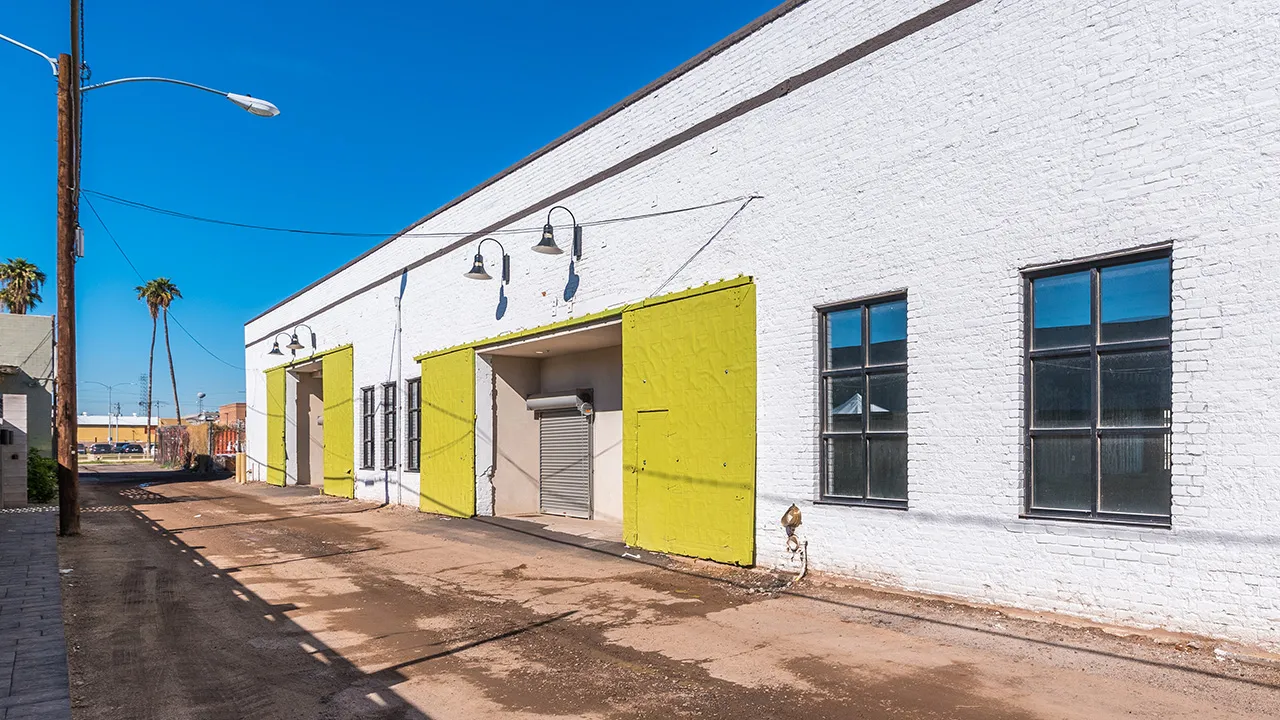 Backside of a white one-story commercial warehouse building with lime green utility doors and black pendant lighting.