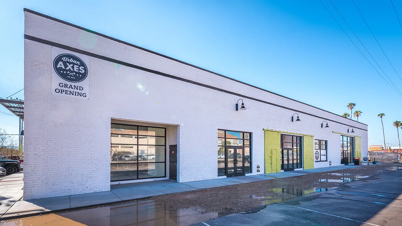 White one-story commercial warehouse building with the number 402 on the side and lime green utility doors and empty parking lot spaces.