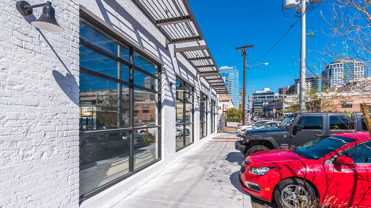 White one-story commercial building with several parked cars out front, and a utility pole with transformers on the sidewalk.
