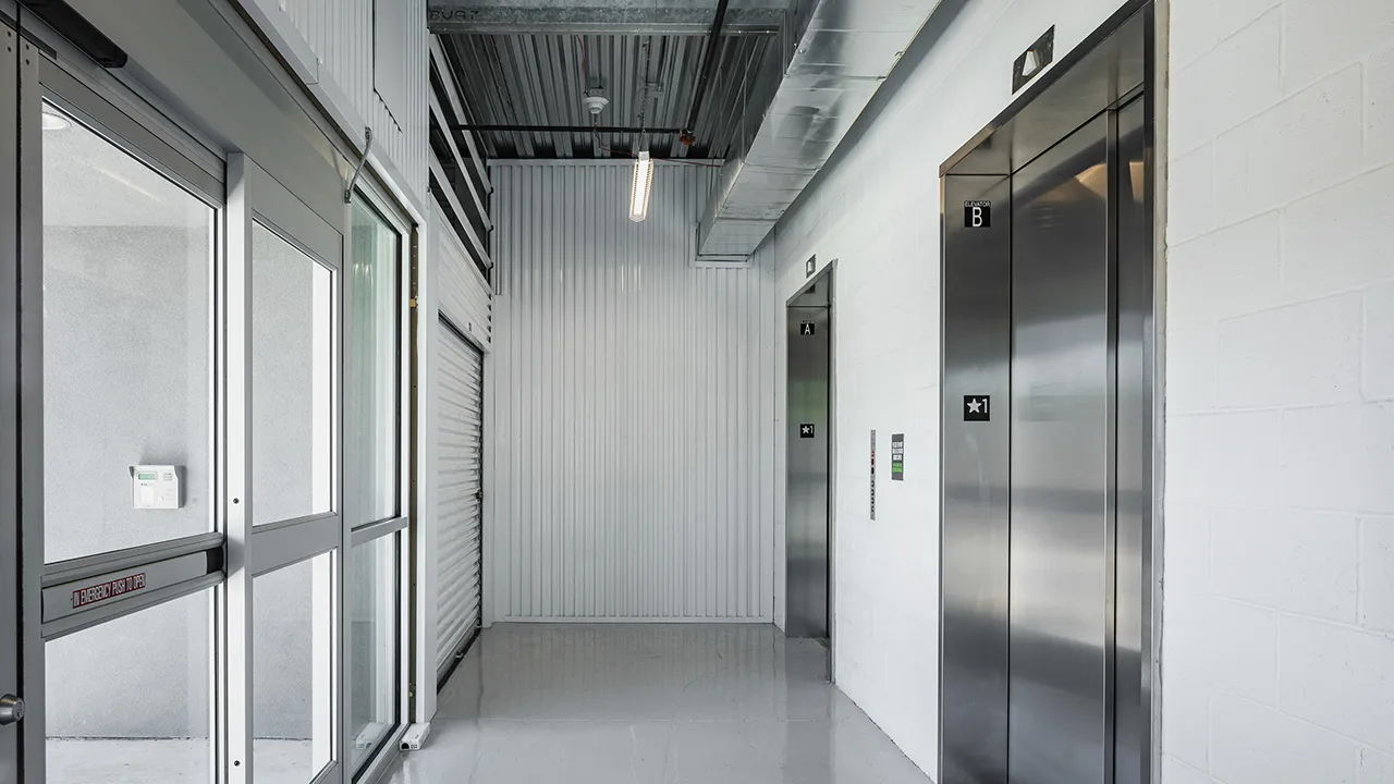 A sliding glass door entryway leading to a set of elevators with shiny polished floor and fluorescent ceiling lights.