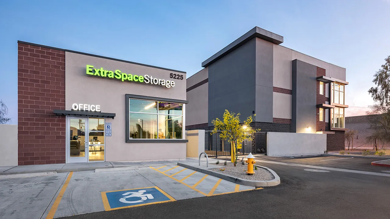 Exterior of an Extra Space Storage facility with a visible office entrance, large window, and handicap parking space in front, under a clear sky at dusk.