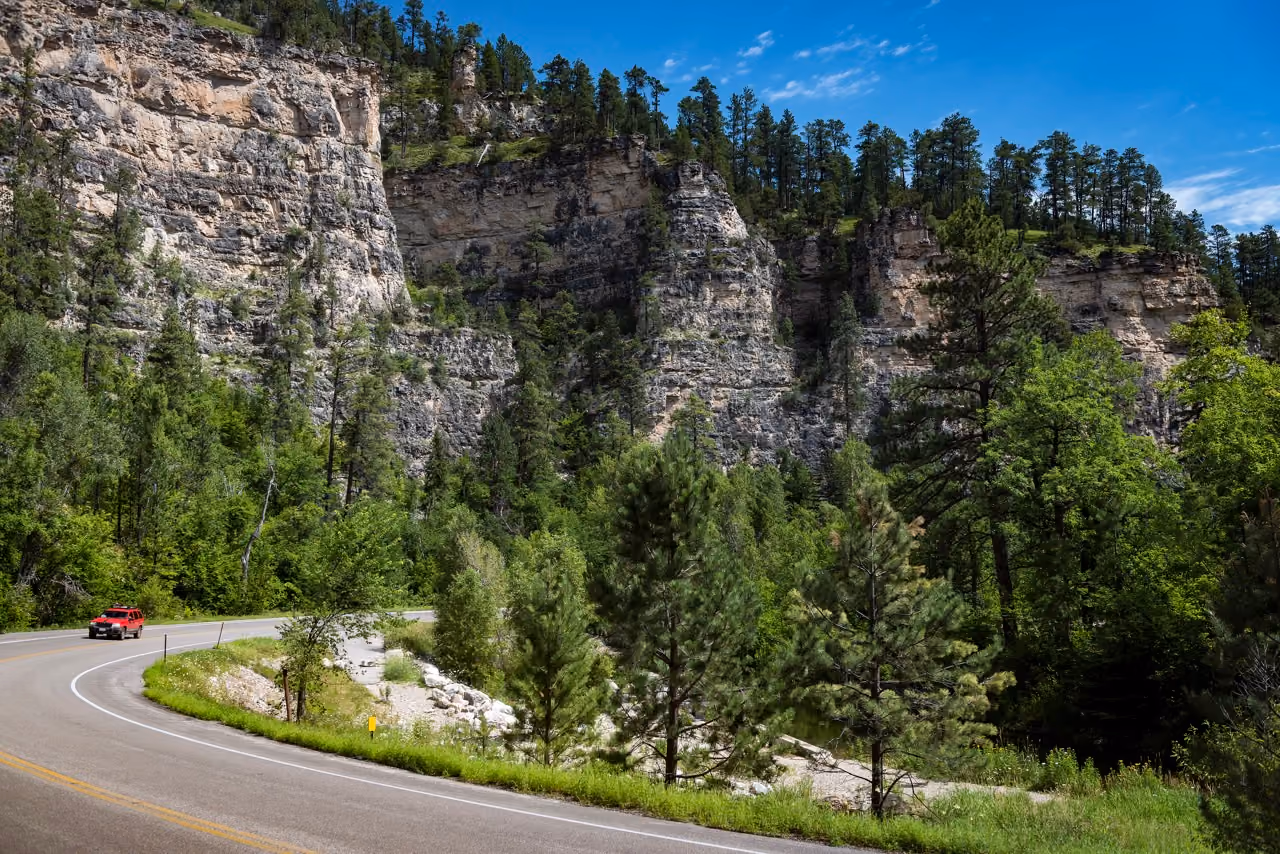 Car driving on Spearfish Canyon Scenic Byway with limestone cliffs in background