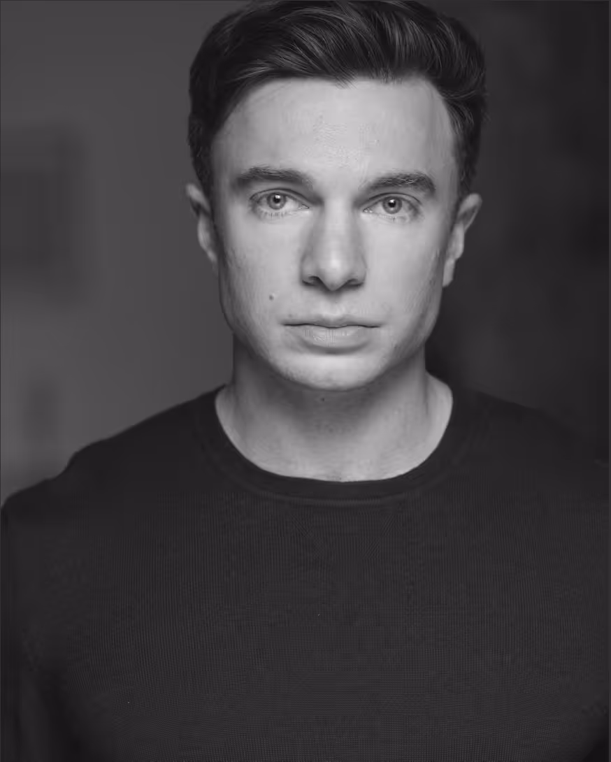 Black and white headshot of a young man with short dark hair wearing a dark shirt, looking directly at the camera.