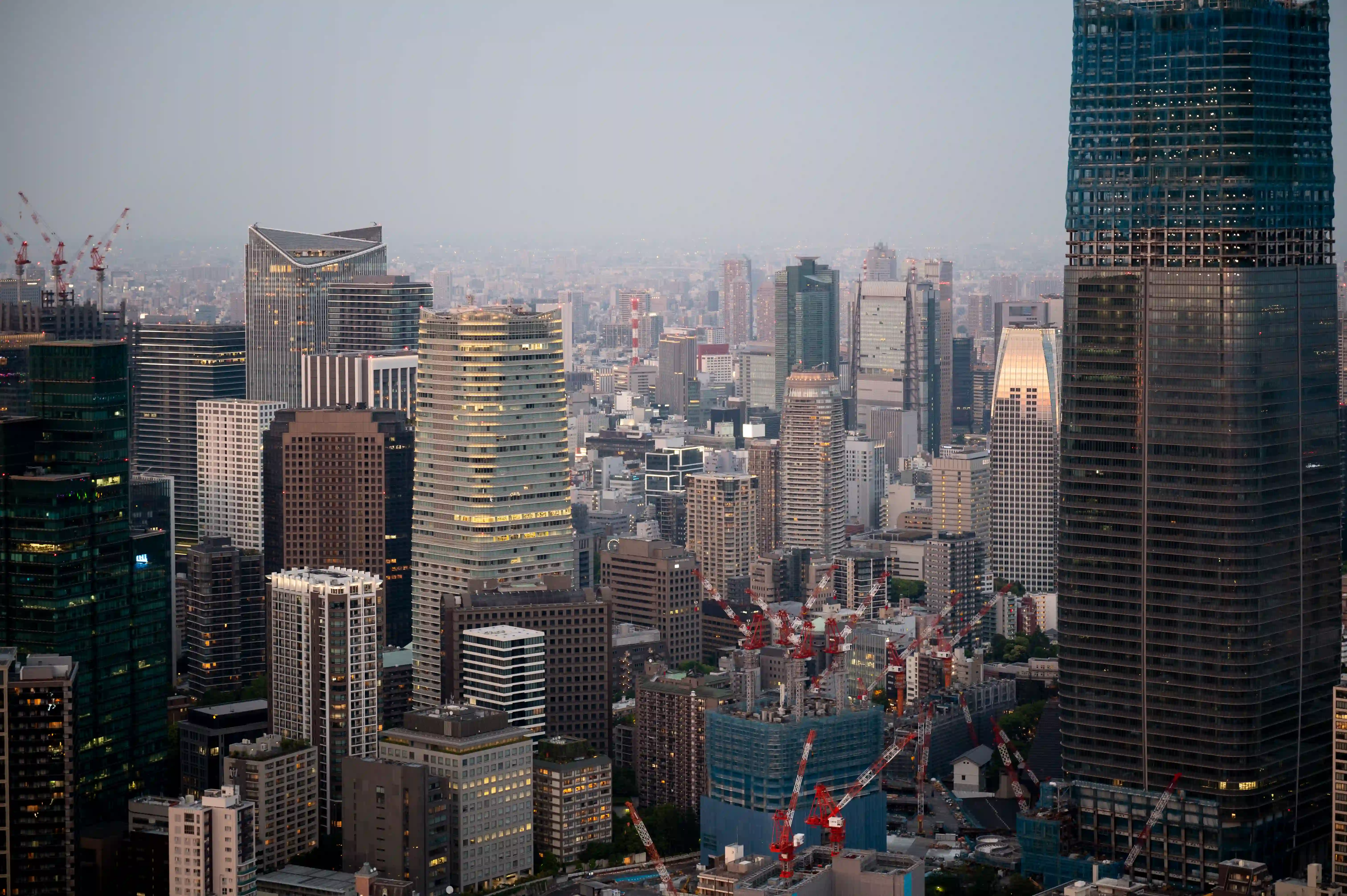 High-angle view of a dense urban cityscape with tall buildings and several construction cranes.