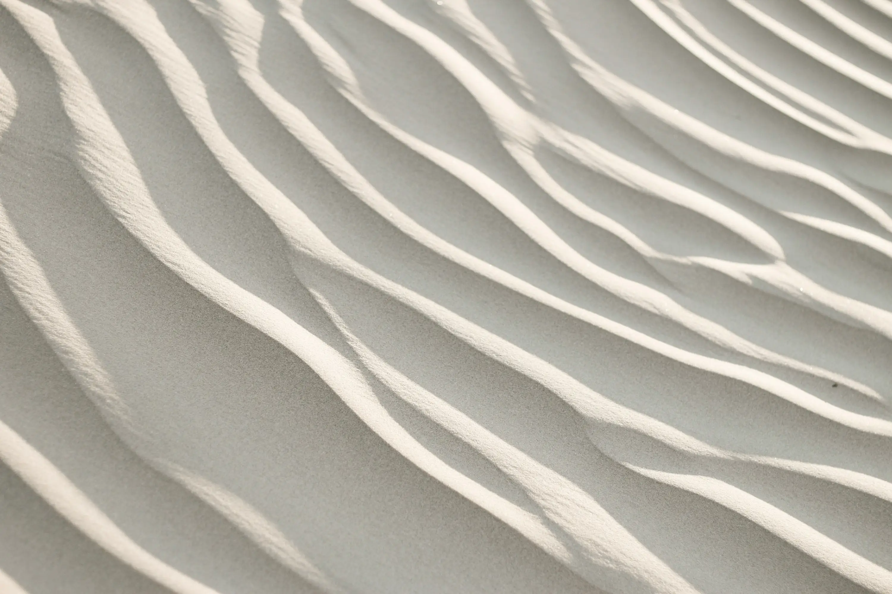 Close-up of light beige sand with rippled patterns formed by wind.
