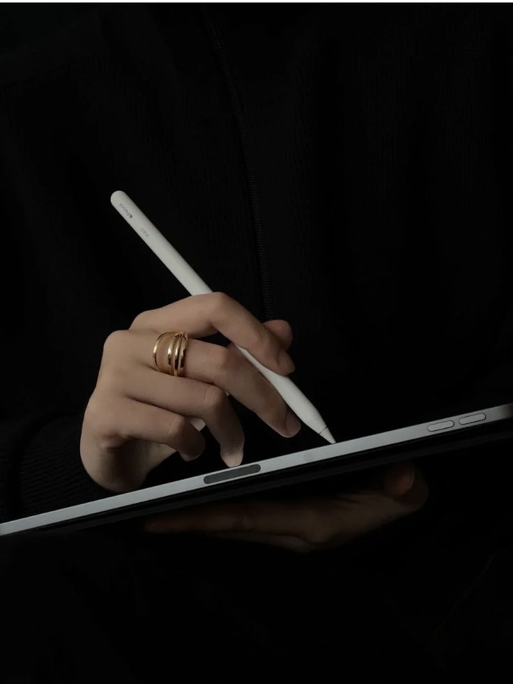 Person wearing black clothing typing on a white Apple laptop while seated on a textured white surface.