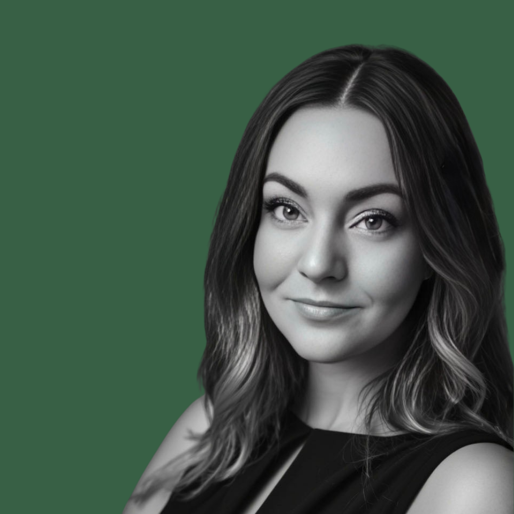 Person wearing black clothing typing on a white Apple laptop while seated on a textured white surface.