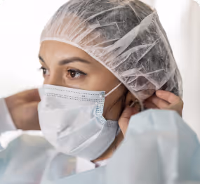 Healthcare worker wearing a disposable hair cap, surgical mask, and protective gown.