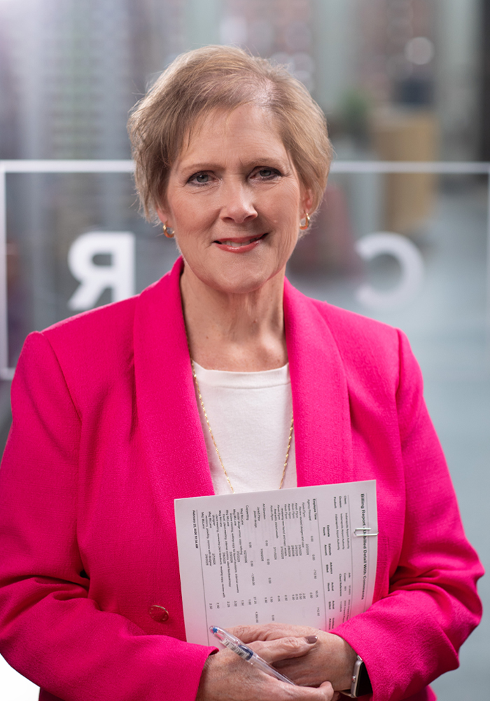 Woman in a bright pink blazer holding a pen and a document with a blurred office background.