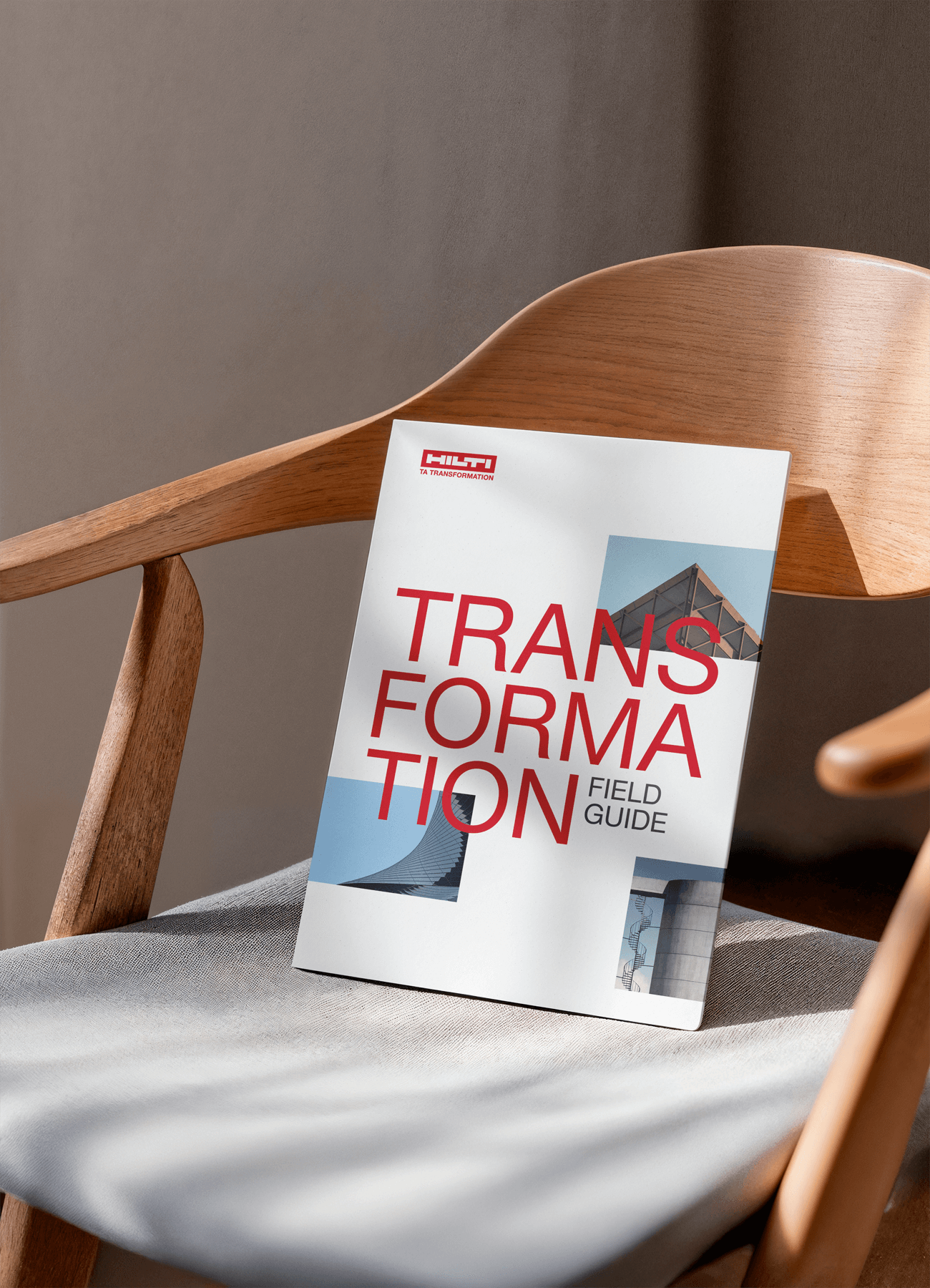 A printed magazine titled "TRANSFORMATION" with bold red text, leaning against the back of a modern wooden chair in soft, dappled sunlight.