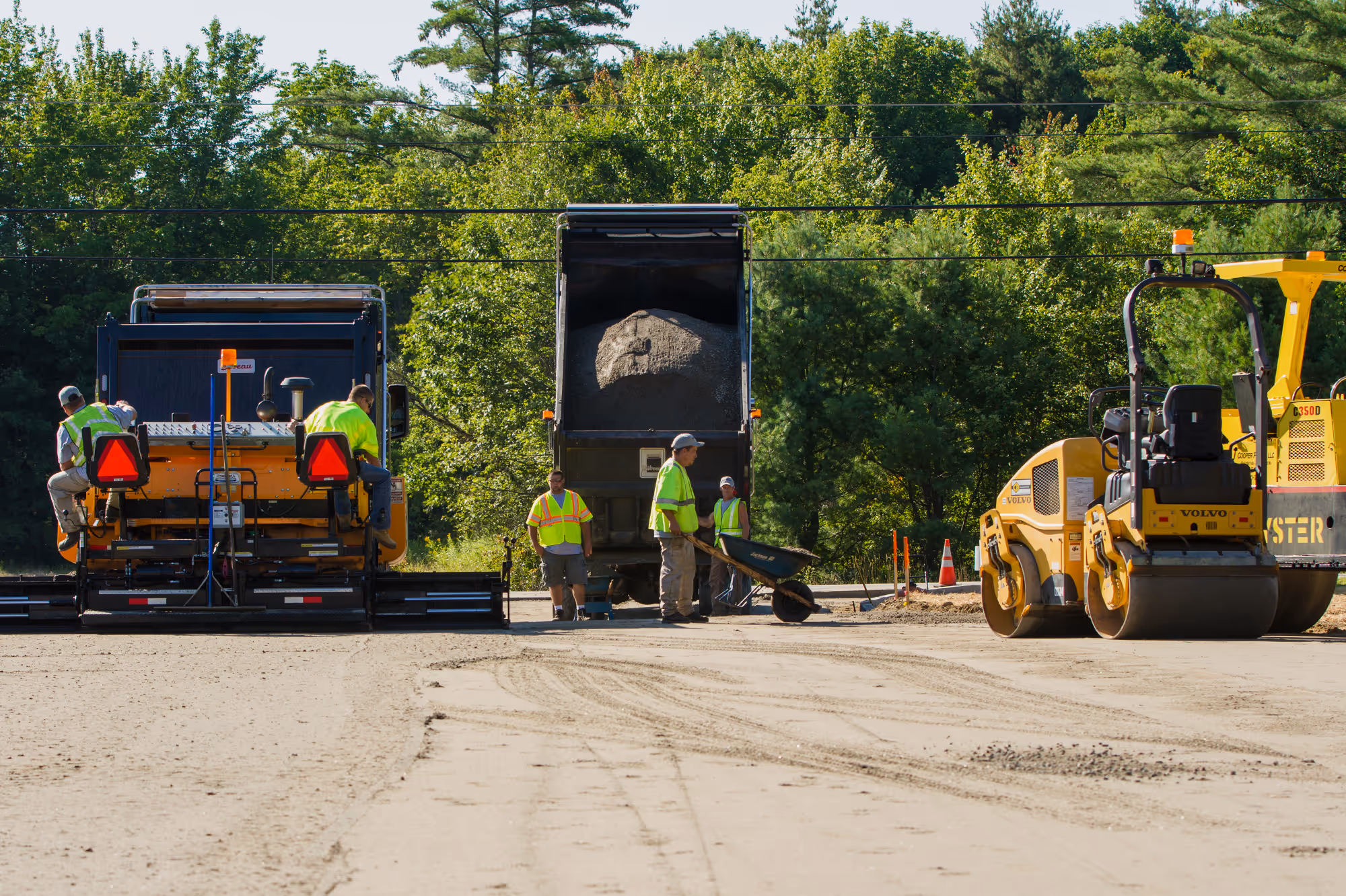Wide view of Cooper Paving crew and equipment on a dirt road