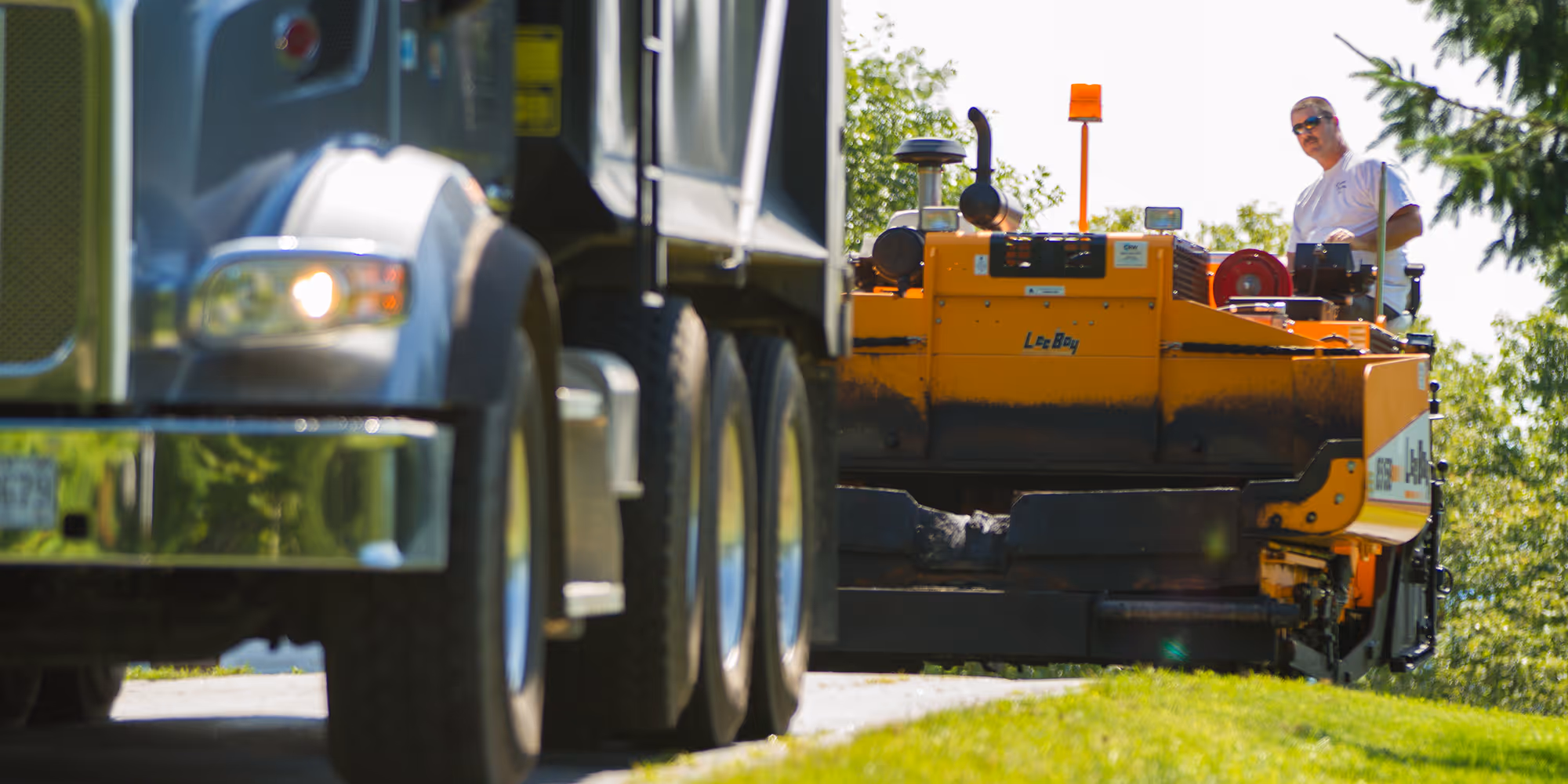 Asphalt paving a driveway with paver and dump truck