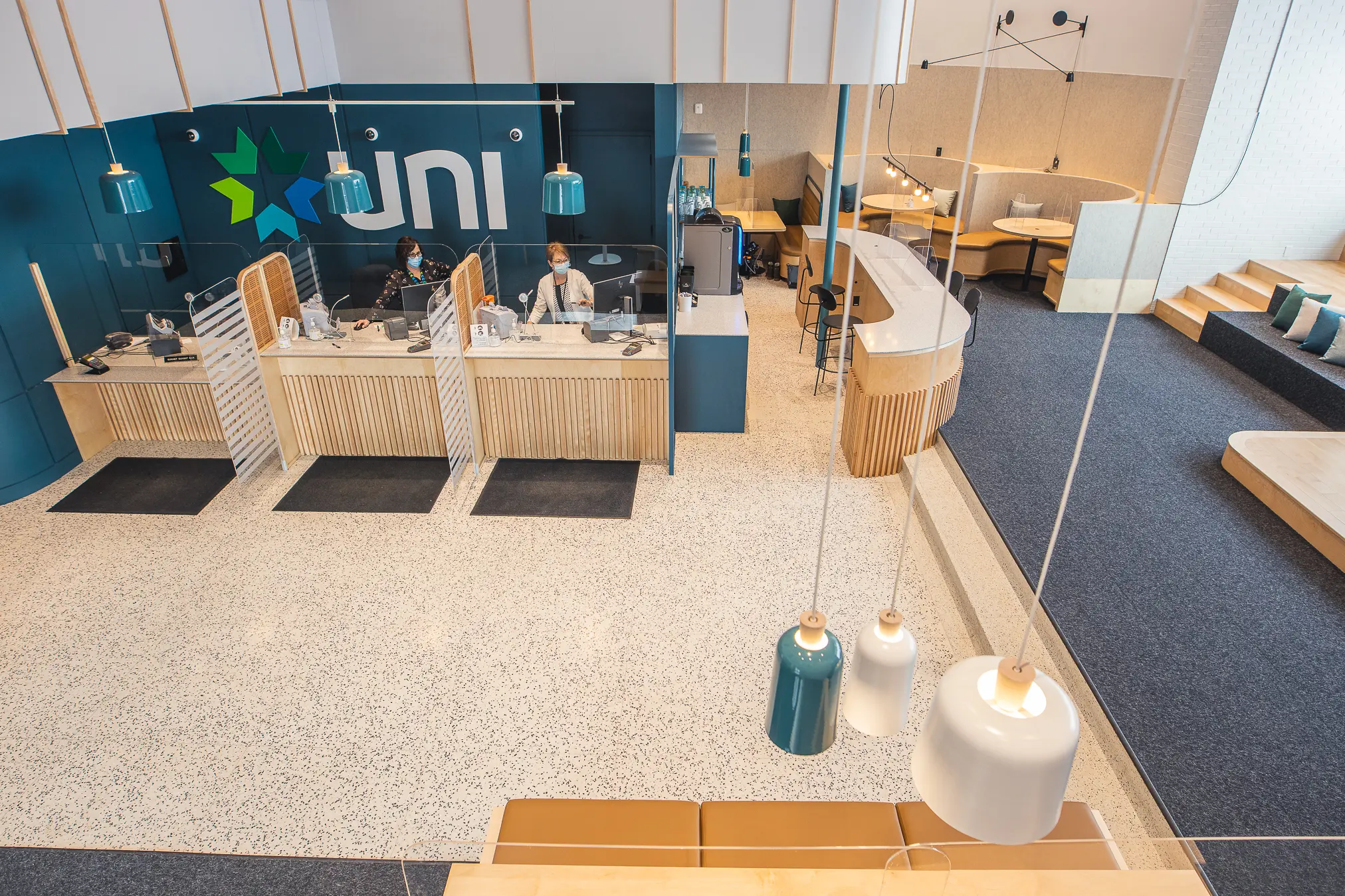 interior view with two masked tellers behind plexiglass, stylish seating areas, and hanging pendant lights.