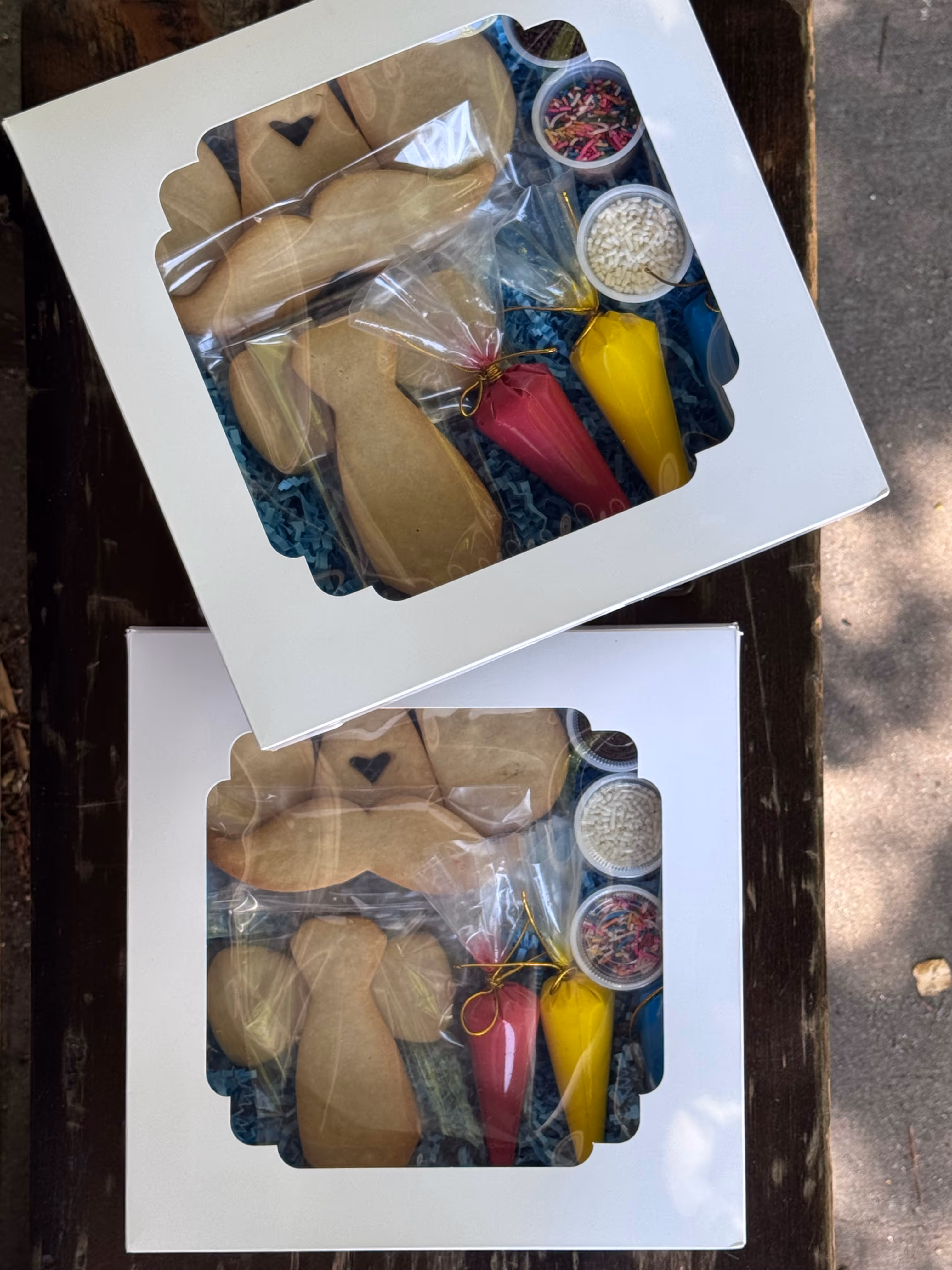 Two cookie decorating kits with angel-shaped cookies, red and yellow icing bags, and sprinkles in white boxes.