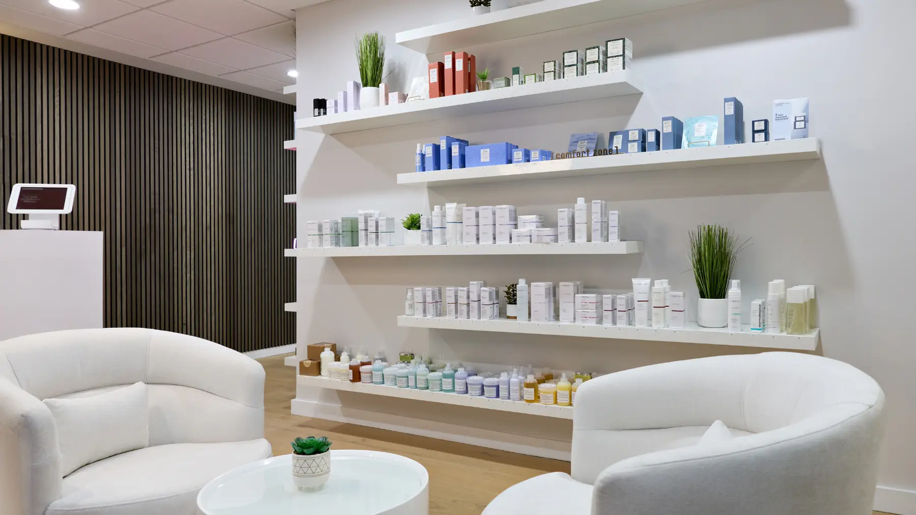 A comfortable waiting area at City Glow beauty salon in Brickell, featuring two white plush chairs and modern white shelves stocked with premium skincare and aesthetic products.