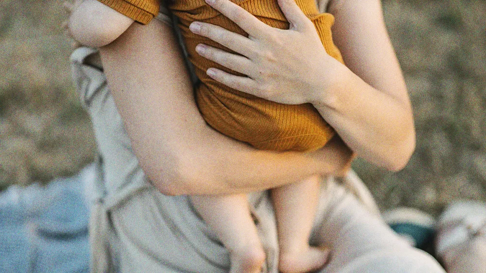 woman's arms holding an infant in an orange jumper