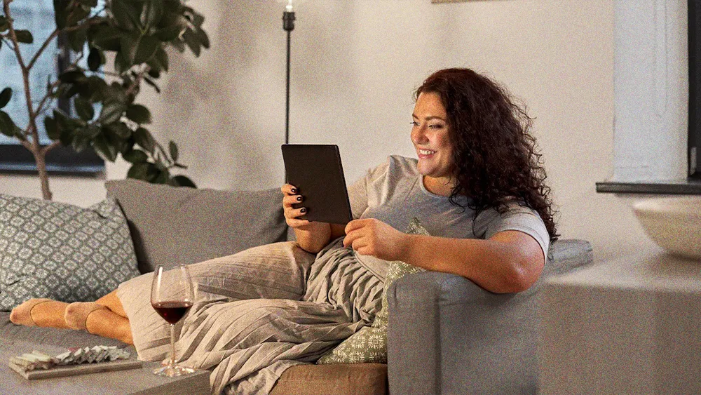woman lounging with a glass of wine, smiling at her tablet