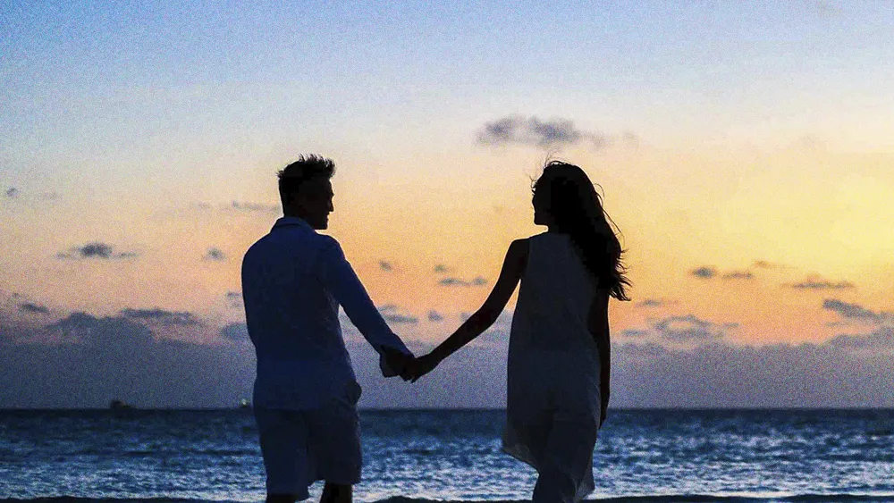 man and woman holding hands watching a beach sunset