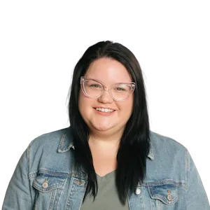 Smiling woman with long dark hair wearing clear glasses, a green shirt, and a denim jacket.