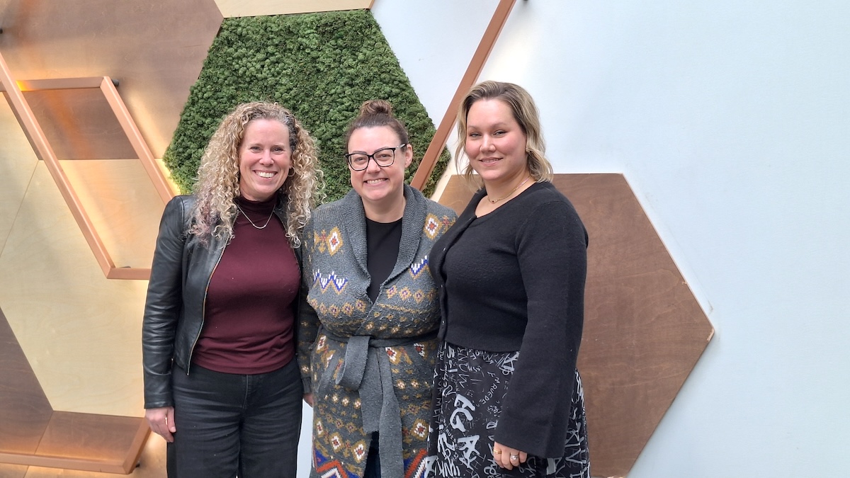myStoria employees Holly, Meaghan, and Carly, standing in front of a modern office wall