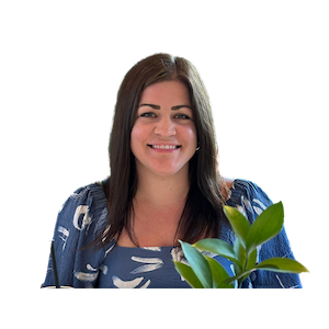 Smiling woman with long dark hair wearing a blue patterned top, with a green plant in the foreground.