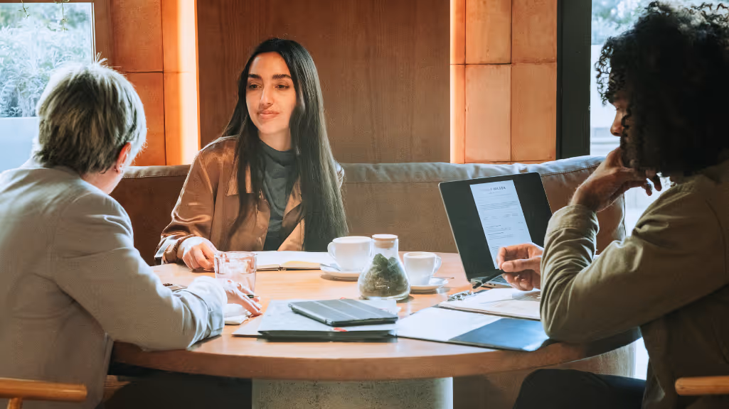 three millennial workers meet in a restaurant or coffee shop over a pile of notes and documents. they appear to be deep in conversation.