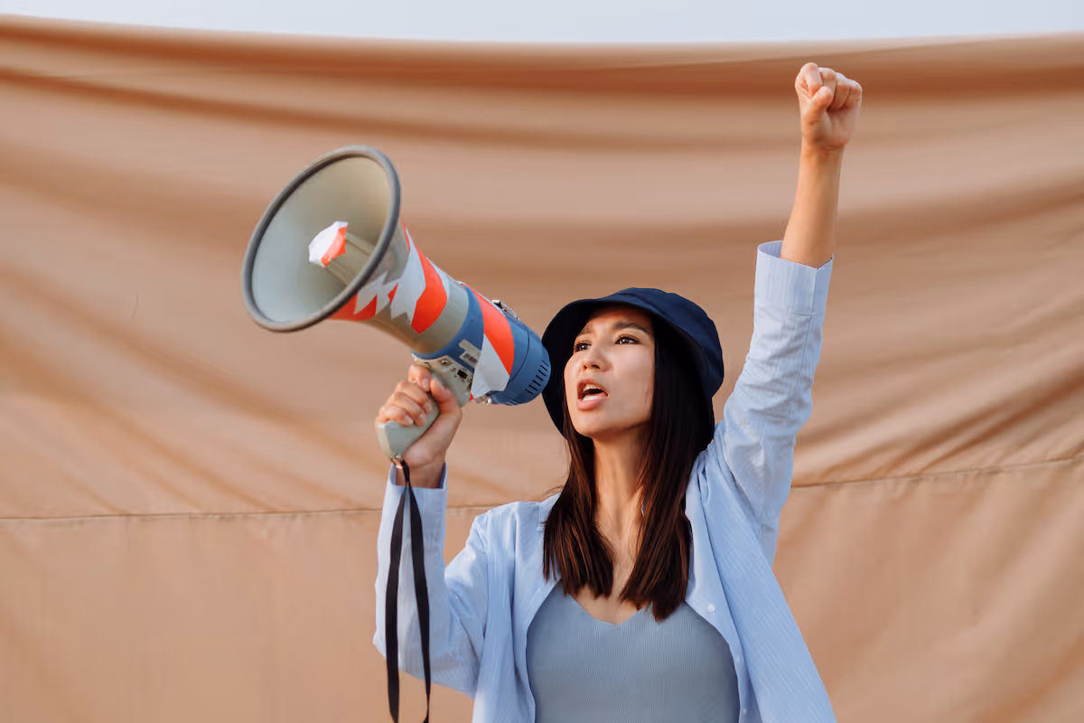A woman raises her fist in the area as she shouts into a megaphone, in front of a canvas backdrop