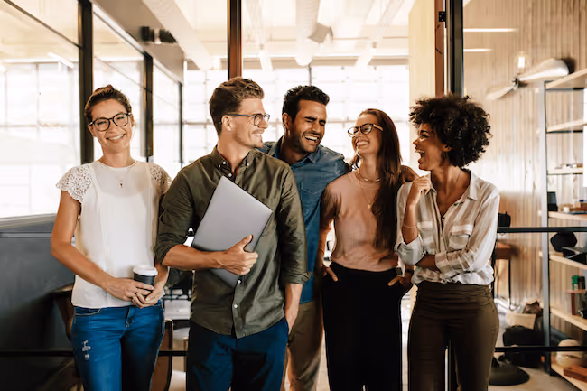 a diverse group of happy millennial employees laugh in an office break room