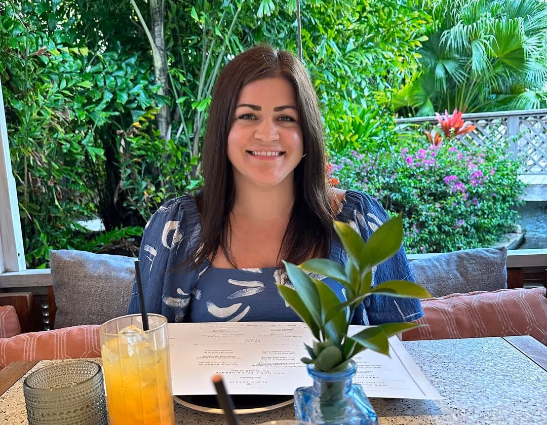 Clare pictured smiling on a leafy restaurant patio, with juice and a menu in front of her