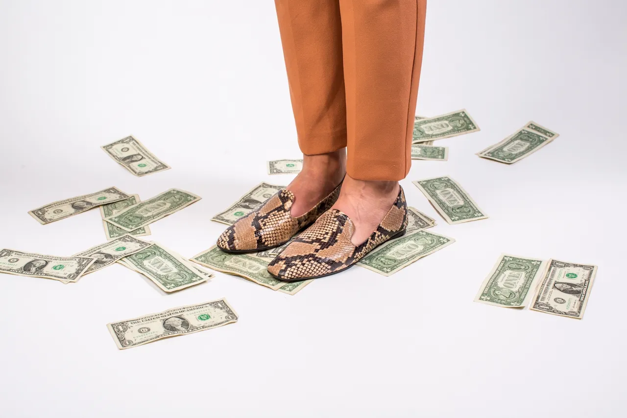 Woman in classy snakeskin shoes standing on a pile of discarded money.