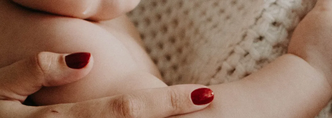 Close-up of clasped hands with red nail polish resting against a textured cream blanket