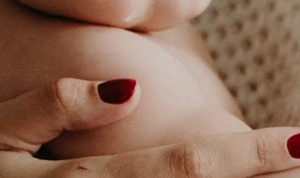 Close-up of clasped hands with red nail polish resting against a textured cream blanket