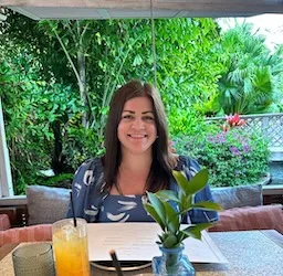 Clare pictured smiling on a leafy restaurant patio, with juice and a menu in front of her