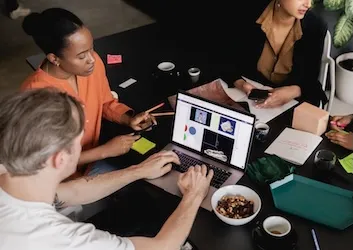 group of office workers gathered around a table with some snacks, participating in a program design process